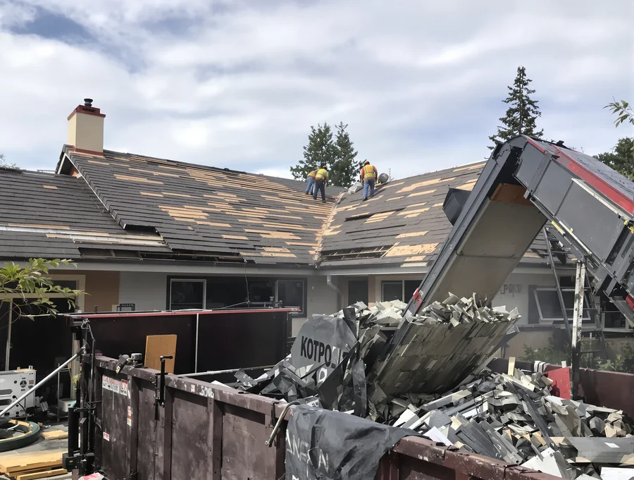 Crew tearing off an old shingle roof into a dumpster